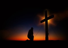 A silhouette of a man kneeling before the empty cross at sunset